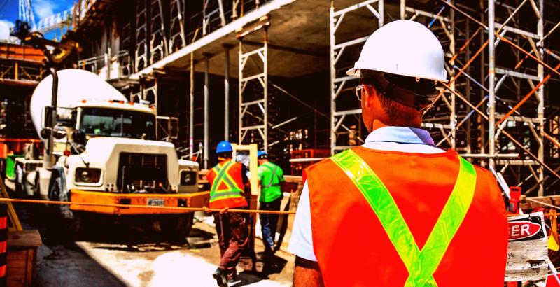 a building under construction with man working while wearing safety vests and a truck is pouring concrete