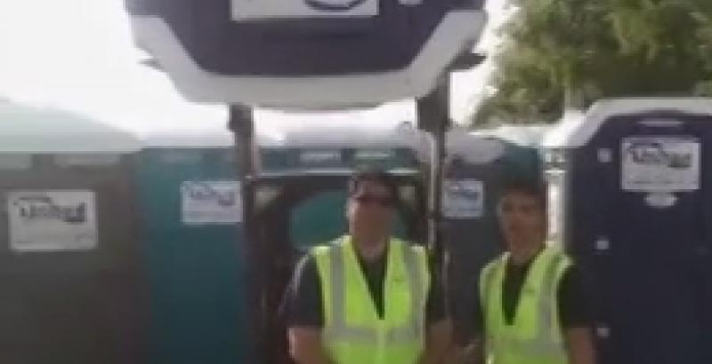 2 male workers wearing safety vests standing around 6 porta potties