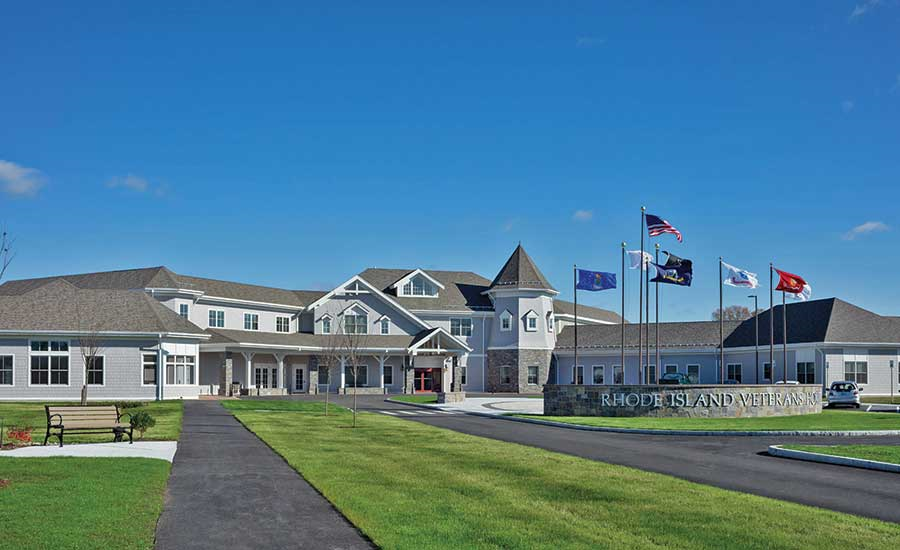 The Rhode Island Veterans Home exterior featuring an expansive building with multiple flags flying in front under a clear blue sky