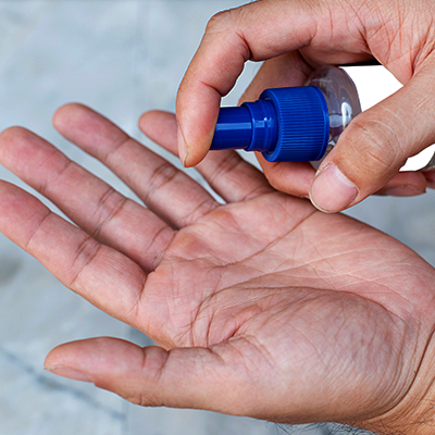 A person applying hand sanitizer from a small blue spray bottle onto their open palm