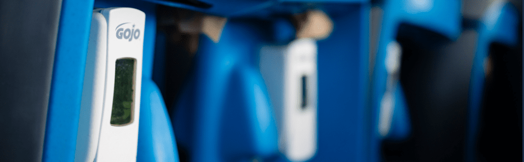 A close-up of a blue hand sanitizer dispenser station with multiple dispensers against a blurred background.