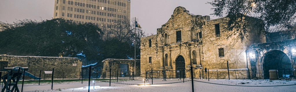 A snowy night at the Alamo illuminated against a backdrop of modern buildings in San Antonio, Texas