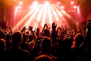 looking toward the stage at a concert, people have their hands in the air and some are filming on their phone