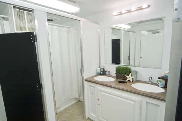 A modern bathroom with a large mirror above a double sink vanity, white cabinets, a white shower curtain, and decorative items under bright lights