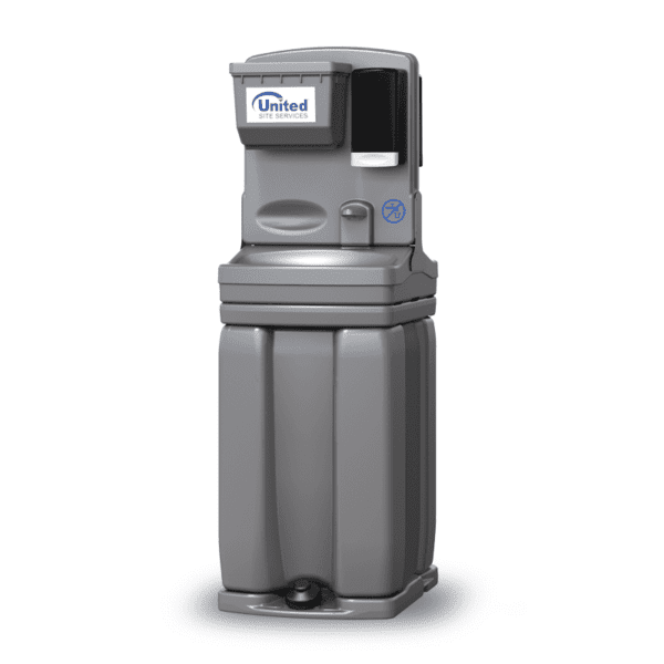 A portable gray handwashing station with a paper towel dispenser and a soap dispenser, set on a grassy area beside a blue portable toilet